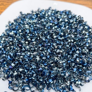 May include: A pile of blue metal shavings on a white surface. The shavings are small and curled, and they have a metallic sheen.