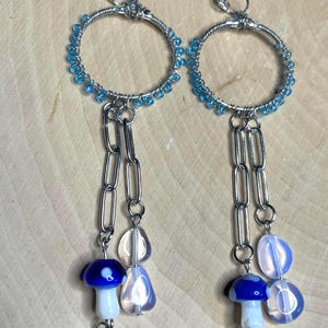 May include: A pair of silver hoop earrings with blue beads and a dangling chain with clear and blue mushroom-shaped beads.