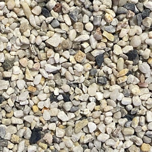 May include: A close-up of a variety of small, smooth, white, grey, and black pebbles. The pebbles are of various sizes and shapes, and they are arranged in a random pattern.