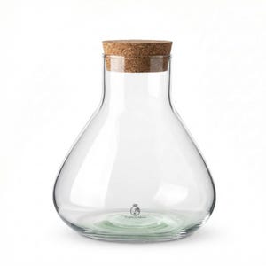 May include: A clear glass bottle with a cork stopper. The bottle has a rounded base and a narrow neck. The cork is light brown. The base of the bottle has a green tint and the words "Tropical Glass".