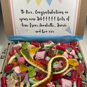 May include: A cardboard box filled with colourful sweets, including gummy worms, gummy bears, and other assorted sweets. The box is decorated with a pink and blue ribbon and a card that reads "To Bex. Congratulations on your new Job!!!!! Lots of love from Annabelle, Jamie and Leo xxx".