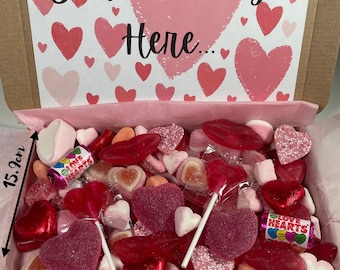 Puede incluir: Una caja de regalo de San Valentín llena de caramelos, incluyendo piruletas en forma de corazón, labios de goma y bombones. La caja mide 21,8 cm de ancho y 15,9 cm de alto, con una tarjeta que dice "Your message Here..." en rosa.