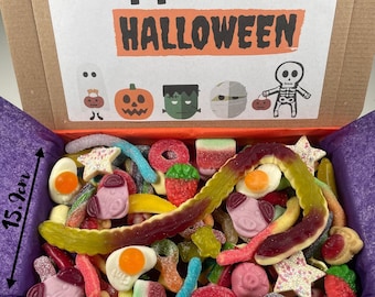 May include: A cardboard box filled with a variety of colorful gummy candies. The box is decorated with a Happy Halloween message and cartoon characters. The box measures 15.2 cm tall and 21.8 cm wide.