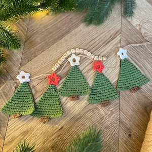 Puede incluir: Guirnalda navideña hecha a mano con cinco árboles de Navidad verdes de ganchillo con troncos marrones. Cada árbol está rematado con una estrella blanca o roja. La guirnalda incluye cuentas de madera con la inscripción "EASY CLY TOYS".