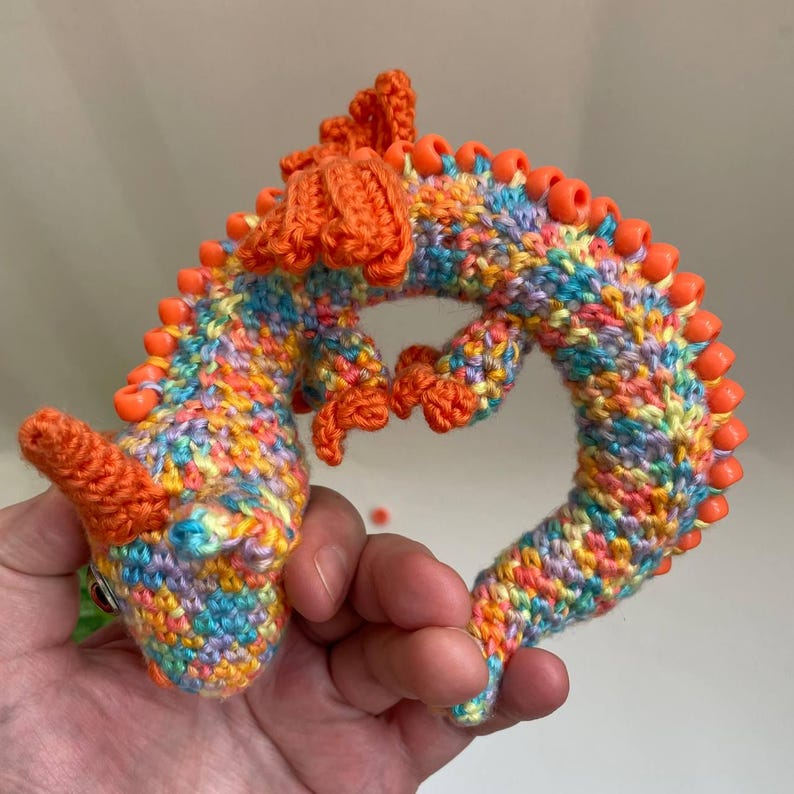 A flexible crochet dragon stretched out straight on a table, showcasing its long, snake-like body that can bend and hold shapes.