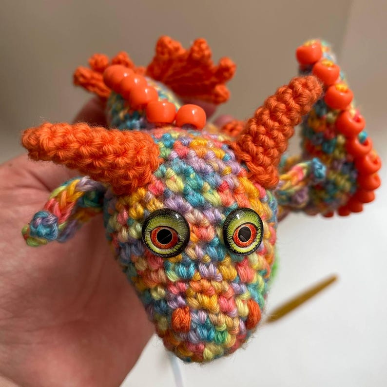 Front view of an orange sensory dragon with a beaded crest and orange beaded wings, coiled on a flat surface, showing its flexible body shape.