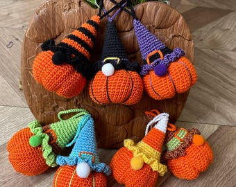 May include: Seven crocheted pumpkin ornaments with different colored hats. The pumpkins are orange and the hats are green, blue, purple, black, and striped. The ornaments are sitting on a wooden surface.