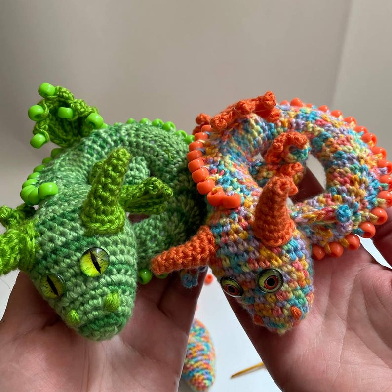 Two completed dragons (orange and green) facing each other on a neutral background, almost touching noses, with a soft, playful composition.