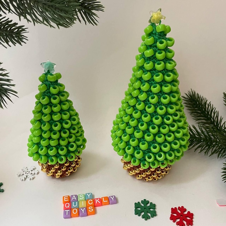 May include: Two handmade Christmas tree ornaments. The trees are green with a gold base and star toppers. The word "EASY QUICKLY TOYS" is spelled out with colorful letter blocks. Decorative snowflakes and pine branches are also visible.