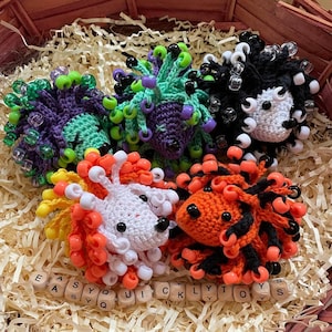 May include: Five crocheted hedgehog figures decorated with colorful plastic beads. The hedgehogs feature various color combinations including purple and green, black and white, orange and black, and white with orange and yellow accents.