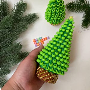 A person's hand gently squeezes the beaded Christmas tree, demonstrating its use