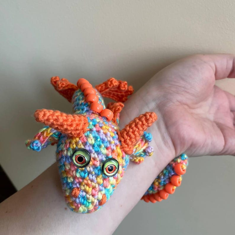 A completed sensory dragon loosely wrapped around a person's fingers, demonstrating how it can be used as a wearable fidget toy.