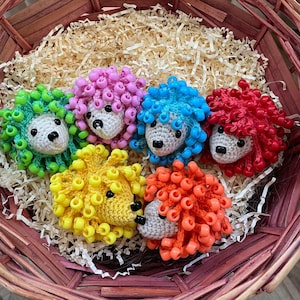 Könnte beinhalten: Sechs handgefertigte Häkel-Igel-Ornamente in einem Weidenkorb. Jeder Igel hat farbige Perlen-„Stacheln“ in Grün, Pink, Blau, Rot, Gelb und Orange. Die Igel haben schwarze Augen und Nasen und liegen auf Holzwolle.