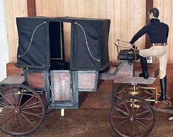 Puede incluir: Maqueta detallada de un carruaje tirado por caballos con techo negro y estructura de madera. Un caballo blanco y negro está enganchado al carruaje. Una figura con camisa negra y pantalón beige está de pie en el carruaje.