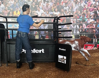 Puede incluir: Un corral de rodeo de metal negro con una figura de toro blanco y negro corriendo fuera del corral. El corral tiene un letrero negro con la palabra "Prefert" en él. El toro es blanco con manchas marrones.