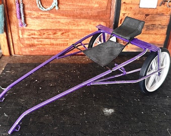 Puede incluir: Carro de caballos de metal morado con dos asientos y dos ruedas. El carro está sobre una estera de goma negra.