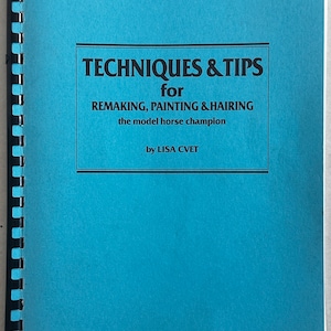 以下が含まれることがあります： リサ・クベット著「モデルホースチャンピオンのリメイク、ペイント、ヘアリングのためのテクニック＆ヒント」というタイトルの青い本の表紙です。