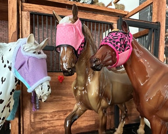 Puede incluir: Tres caballos de juguete con mosquiteras. El caballo de la izquierda tiene una mosquitera morada, el caballo del medio tiene una mosquitera rosa con lunares blancos y el caballo de la derecha tiene una mosquitera rosa con estampado de leopardo negro.