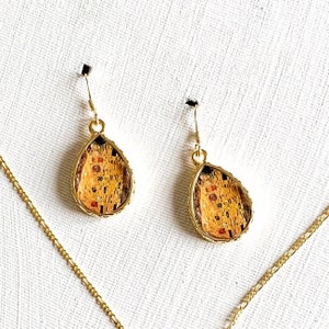 Könnte beinhalten: Goldene Tropfenohrringe mit einem Gemälde von Der Kuss von Gustav Klimt in jedem Ohrring.