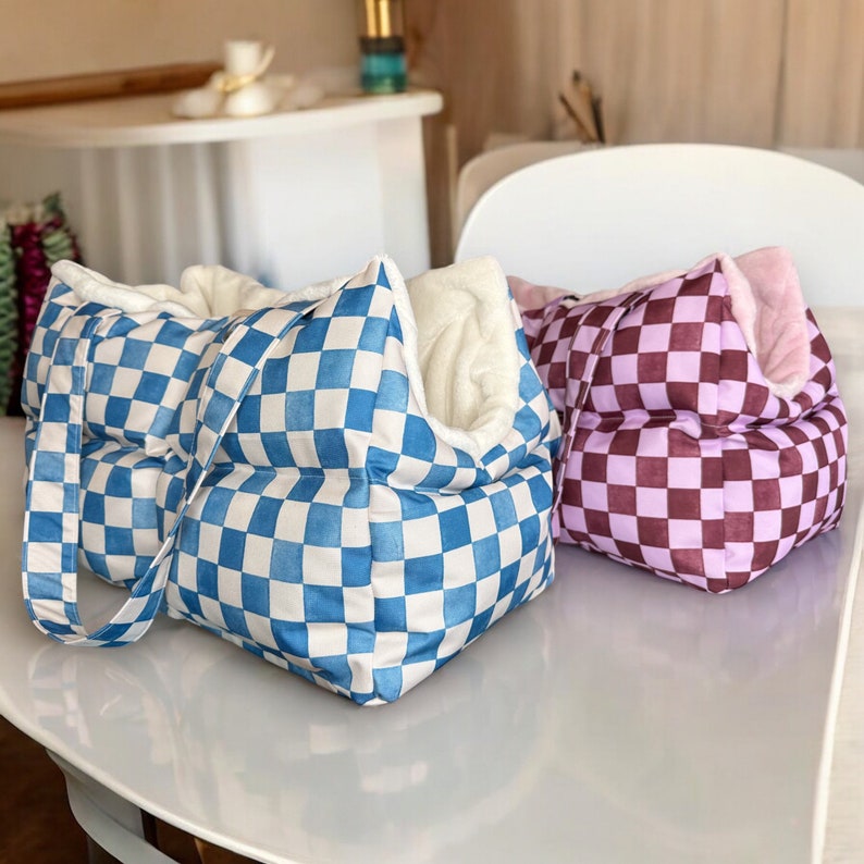 May include: Two checkered pet beds, one blue and white and one pink and white. The blue and white bed has a handle and is made of a soft, quilted fabric. The pink and white bed is also quilted and has a fluffy white lining.