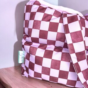 May include: A pink and brown checkered tote bag with a white fluffy lining and a white strap. The bag has a small tag that says "Gain" on it.