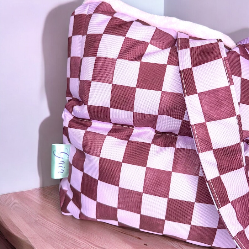 May include: A pink and brown checkered tote bag with a white fluffy lining and a white strap. The bag has a small tag that says "Gain" on it.