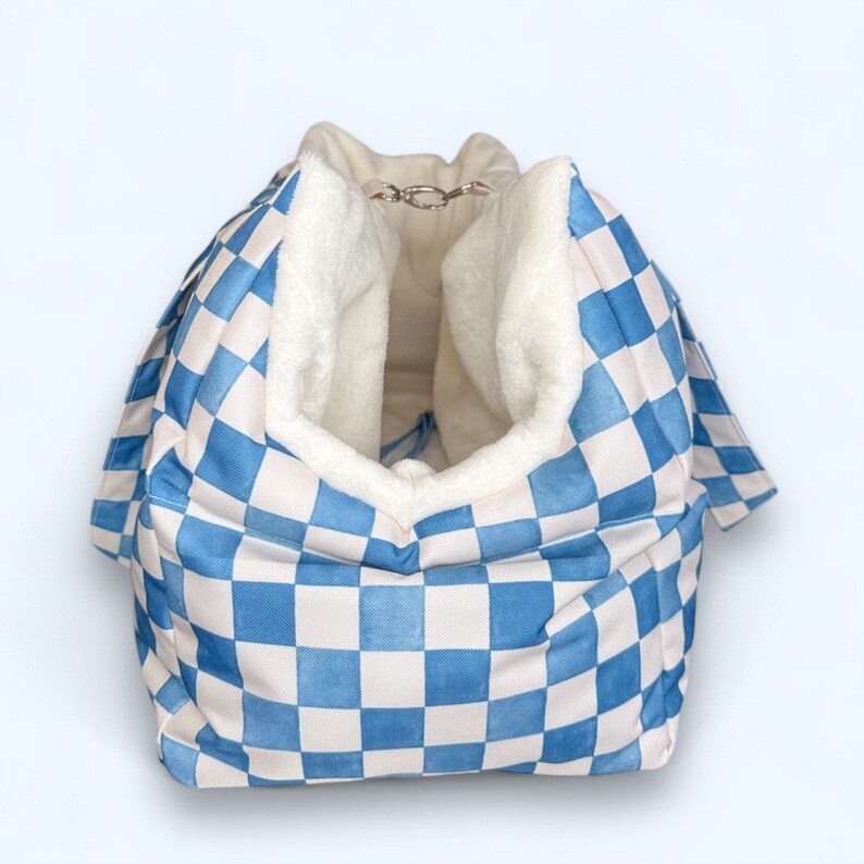 May include: A blue and white checkered pet bed with a soft white fleece lining. The bed has a drawstring closure at the top.