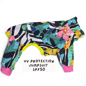 Puede incluir: Un mono para perro negro y blanco con estampado floral tropical. El mono tiene un ribete amarillo y puños rosas. El texto "UV PROTECTION JUMPSUIT SPF50" está impreso en la parte delantera.