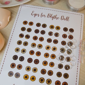 May include: A white card with the text "Eyes for Blythe Doll" and "Anri Customised Dolls" printed on it. The card features a grid of 42 brown doll eyes and a pile of clear plastic doll eyes.