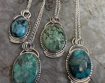 Peut inclure: Quatre colliers pendentifs en argent avec des pierres ovales en turquoise. Les pierres présentent des nuances de bleu et de vert, avec des motifs de matrice foncés. Chaque pendentif a un cadre argenté décoratif et est suspendu à une chaîne délicate.