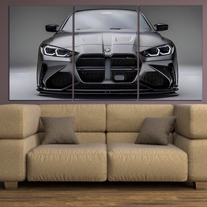 Puede incluir: Impresi&oacute;n en lienzo de tres paneles que muestra un coche deportivo BMW gris. El coche est&aacute; centrado, mostrando su parte delantera con los faros encendidos. La impresi&oacute;n cuelga sobre un sof&aacute; beige con dos cojines, contra una pared p&uacute;rpura.