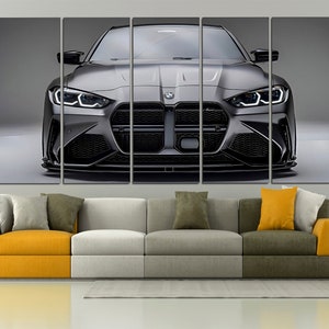 Puede incluir: Impresi&oacute;n en lienzo de un coche deportivo gris, visto de frente. El coche tiene detalles en negro y faros brillantes. La obra de arte se exhibe sobre un sof&aacute; moderno con cojines amarillos y grises.