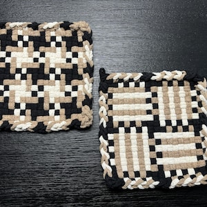 May include: Two square woven pot holders with a black, white, and tan checkered pattern. The pot holders have a braided border.