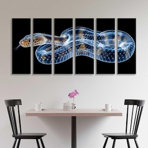 Puede incluir: Una obra de arte en lienzo de varios paneles que presenta una ilustración detallada de una serpiente sobre un fondo negro. La serpiente tiene un cuerpo azul translúcido, marcas marrones y beige y una lengua bífida. La obra de arte se exhibe encima de una mesa con sillas.