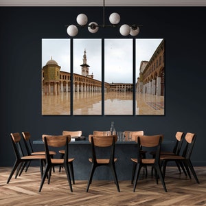 Op de afbeelding: Een vierdelige canvas print met een historische moskee met een minaret en gewelfde colonnades. Het kunstwerk wordt getoond boven een eettafel met houten stoelen, waardoor kunst en meubels worden gecombineerd.