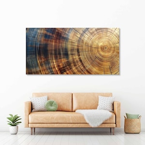 May include: A rectangular wall art print featuring a close-up of a tree trunk cross-section. The artwork displays concentric rings in shades of brown, gold, and blue, creating a natural, textured pattern. The print is mounted above a tan leather sofa.