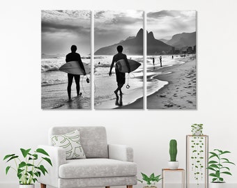 May include: Black and white photo of two surfers walking on a beach with their surfboards. The beach is empty except for a few other people in the distance. The photo is split into three panels.
