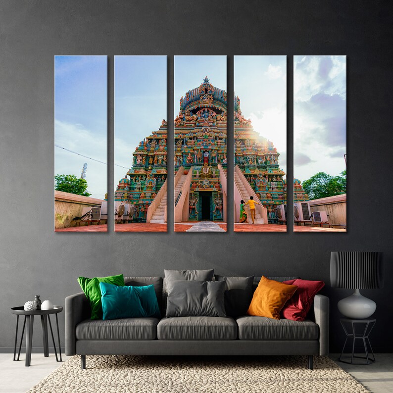 May include: A colorful, multi-level Hindu temple with intricate carvings and statues. The temple is set against a blue sky with white clouds. Two people are walking away from the temple.