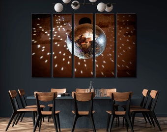 May include: A five-piece canvas print set featuring a disco ball hanging from the ceiling, with light reflections on the brown background. The print set is displayed on a dark blue wall above a dining table with six chairs.