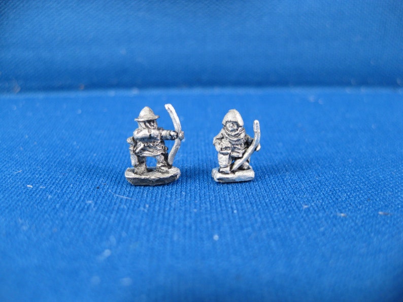 May include: Two miniature metal figures of archers, one with a raised bow and arrow, the other with a lowered bow and arrow. Both figures are wearing hooded cloaks and helmets.