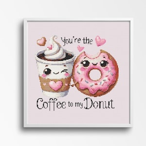 May include: Cross-stitch art featuring a coffee cup and a donut, both with smiling faces and holding hands. The coffee cup has whipped cream and a heart, and the donut is pink with sprinkles. Text reads "You're the Coffee to my Donut."