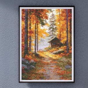 May include: Framed cross-stitch art depicting an autumn forest scene. The artwork features a path leading to a small cabin, surrounded by trees with vibrant orange and yellow foliage. The scene is set in a forest with a bright, sunny sky.