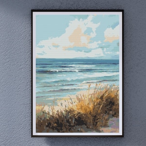 Op de afbeelding: Ingelijste kunstafdruk van een strandscène. Het kunstwerk toont een kustlandschap met een blauwe oceaan, lucht en wolken. De voorgrond toont goudbruin strandgras. De print zit in een zwart frame, perfect voor kustdecoratie.