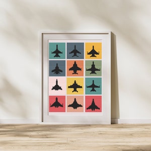 May include: A framed art print showing a grid of twelve squares, each with a black silhouette of a jet aircraft. The squares are in various colours, including teal, orange, yellow, and pink. The artwork is in a white frame.
