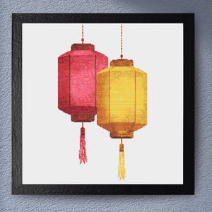 May include: A framed print featuring two hanging lanterns. One lantern is red, the other is yellow. Both have a rectangular shape with a tassel at the bottom. The lanterns are suspended from a dotted line.
