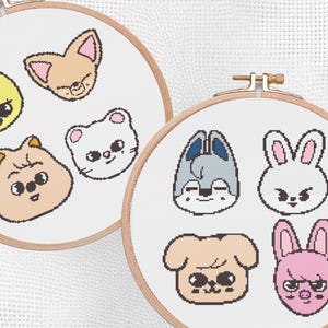May include: Two cross-stitch hoops featuring cartoon animal faces. One hoop has a yellow chick, a tan cat, a tan hamster, and a white cat. The other hoop has a gray wolf, a white bunny, a tan dog, and a pink bunny.