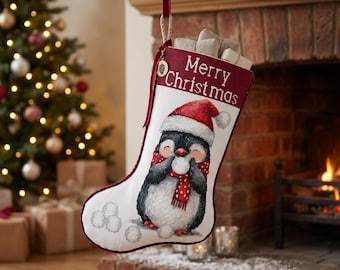 May include: A white Christmas stocking with a dark red trim and the text Merry Christmas embroidered at the top. The stocking features a graphic of a penguin wearing a red Santa hat and a red polka-dot scarf, holding a snowball with more snowballs below.
