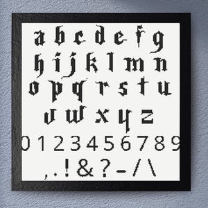 May include: Black framed cross-stitch sampler featuring the alphabet, numbers, and punctuation marks. The letters and numbers are in a gothic style, stitched in black thread on a white background. The sampler is a decorative piece.