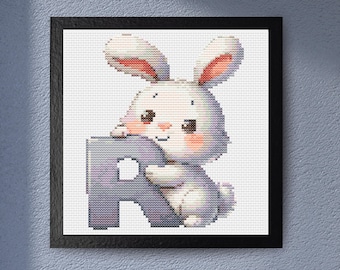 May include: A framed cross-stitch artwork featuring a cute bunny hugging the letter "R". The bunny is white with pink accents on its ears and cheeks. The letter "R" is a soft purple. The artwork is set against a white background.