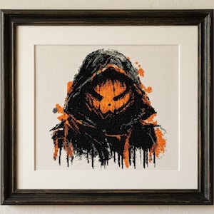 Puede incluir: Una obra de punto de cruz enmarcada que muestra una figura encapuchada con un rostro naranja brillante similar a una calabaza. El diseño utiliza hilo negro y naranja sobre un fondo de tela blanca, con salpicaduras y goteos de pintura.